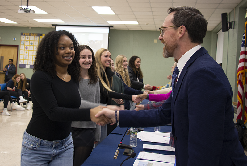 A line of high school girls shake hands with school officials.