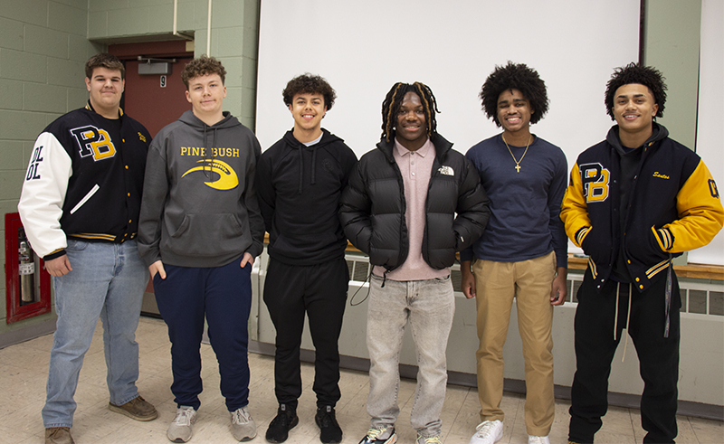 Six young men, all high school football players, stand together and smile.