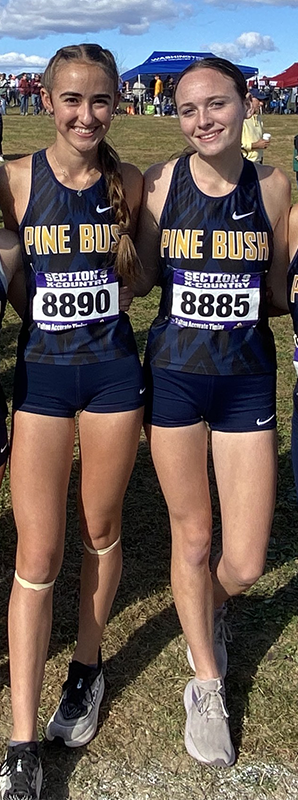 Two young women in blue and gold uniforms link their arms and smile.