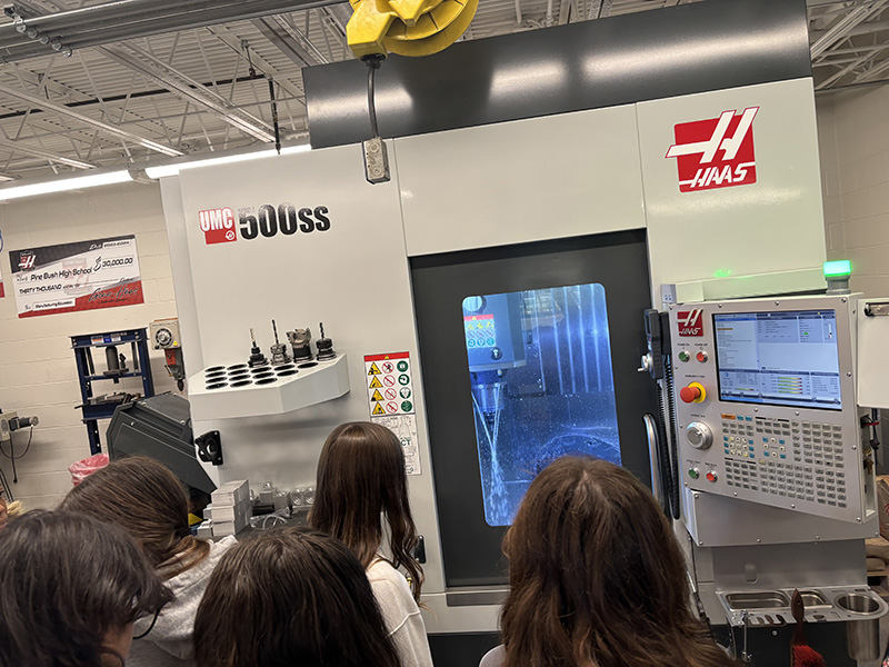 A group of middle school students look at a machine that is cutting a material with water.