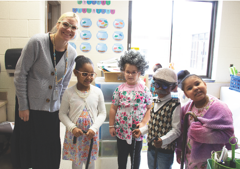 A teacher, dressed as an old woman, stands with four of her kindergarten kids, also dressed as old people.