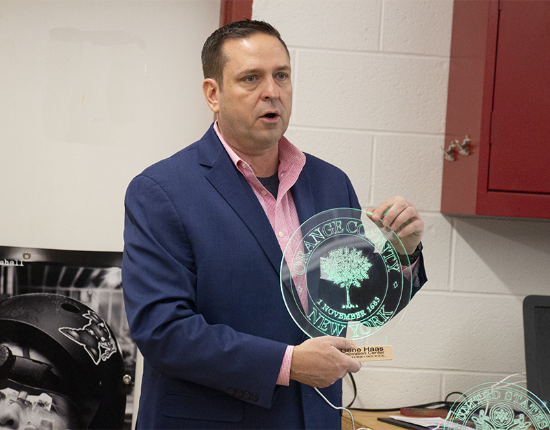 A man wearing a pink shirt and blue blazer holds an etched glas that says Orange County.