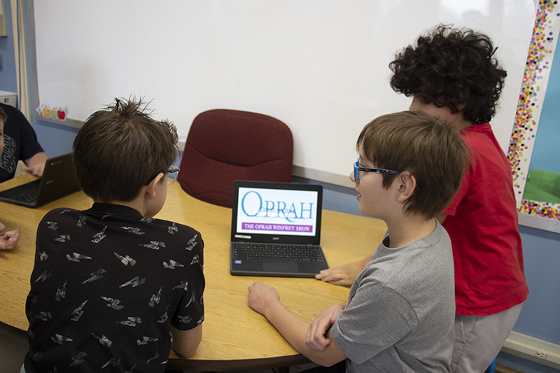 Three students sit around a chromebook watching a video about Oprah Winfrey.