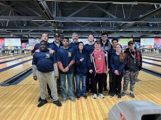 A group of 10 high school kids and two adults stand for a picture in a bowling alley.