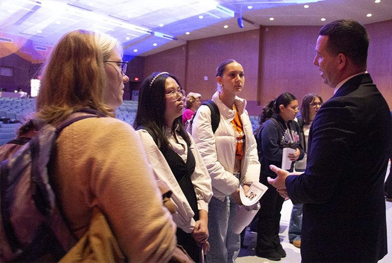 Three high school students talk to a man in an auditorium.