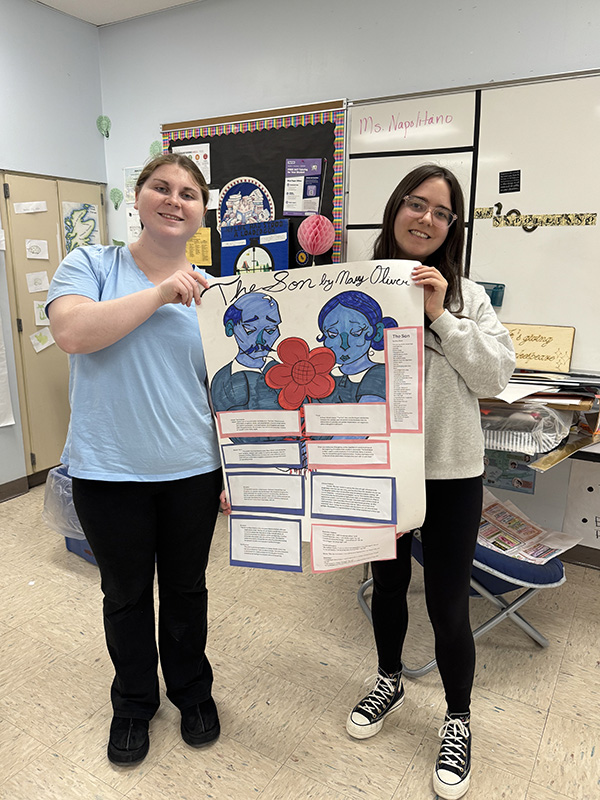 Two high school senior girls hold up a project they made about a poem.